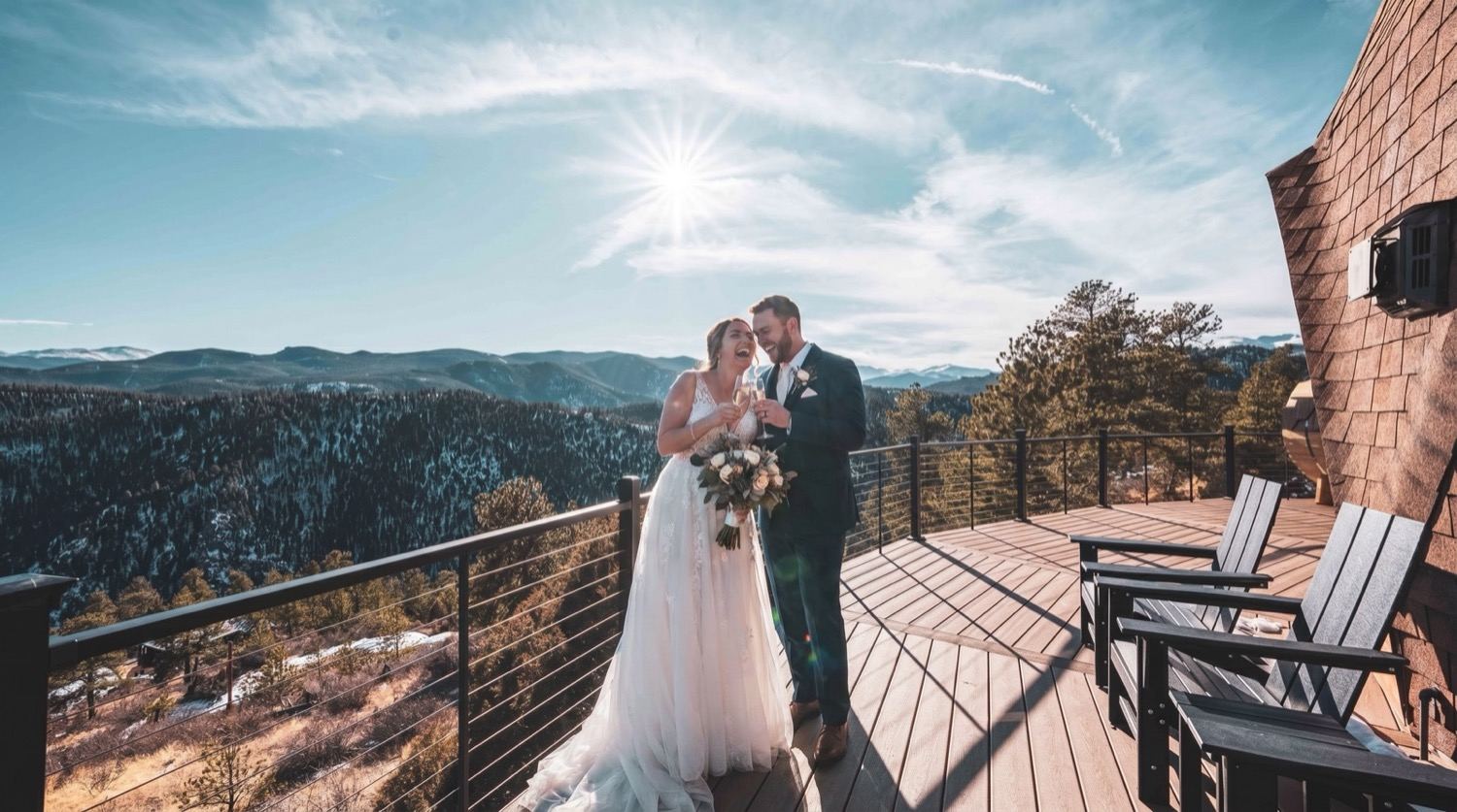 A couple exchanging vows on the wraparound deck with the mountain range behind them